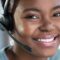 Close-up image of a young woman smiling and wearing a contact center headset.