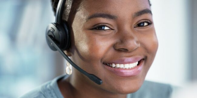 Close-up image of a young woman smiling and wearing a contact center headset.