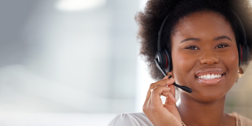 Image of a smiling young Black woman wearing a headset, which she is adjusting with one hand.