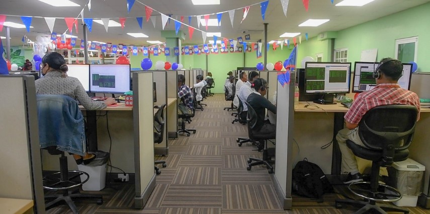 A room full of cubicles, with image centered on the aisle. Multi-colored flags are strung across the ceiling.